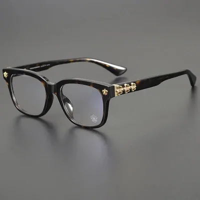 A pair of square tortoiseshell eyeglasses with clear lenses and small gold studs on the temples, on a plain grey background.