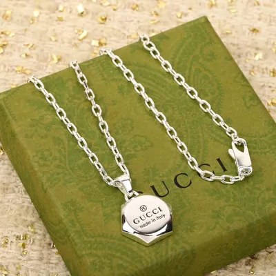 A silver chain necklace with a hexagonal engraved pendant, laid out on a green patterned gift box.