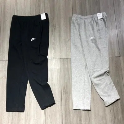 A pair of black track pants and a pair of grey track pants laid flat side by side on a wooden floor.
